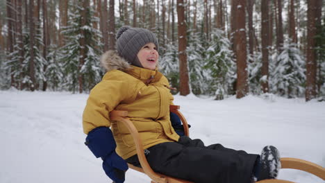 Portrait-of-a-smiling-boy-3-4-years-old-in-slow-motion-who-rides-a-sled-in-a-snowy-forest-in-winter